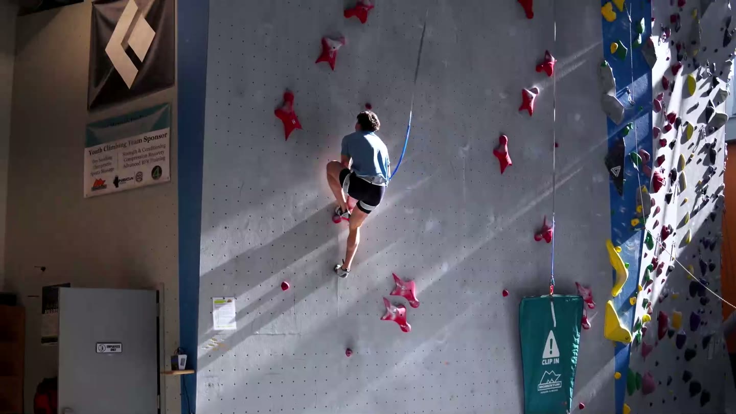 A climber moving dynamically on the red holds of a speed wall